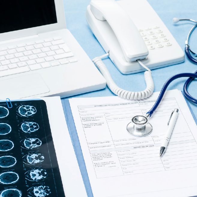 Medical workspace setup with a laptop, phone, stethoscope, brain scan images, and medical documents,